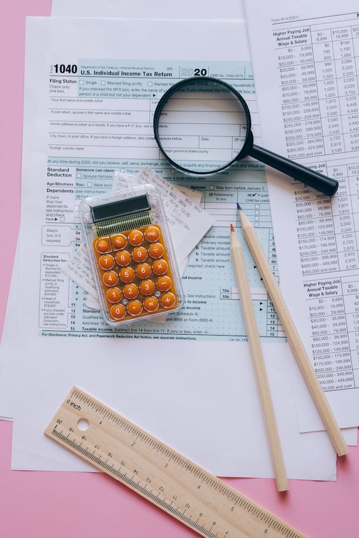 Magnifying glass, calculator, pencils on tax forms with pink background. Ideal for finance or education themes.
